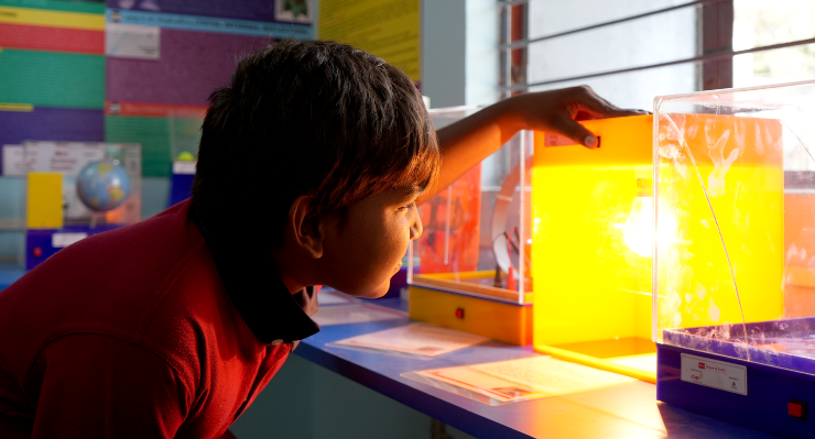 A schoolboy looks at a lit lamp through a box