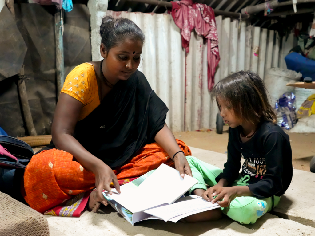 A woman and a child sit on the ground. The woman is flipping through the pages of a notebook.