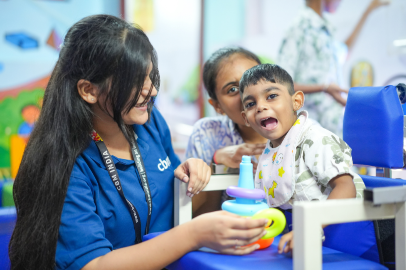 A therapist plays with a young child during a therapy session while another woman sits behind the child.
