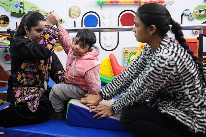 Two women help a small child during a physiotherapy session