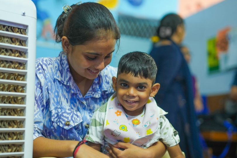 A girl looking at a smiling little boy sitting on her laps